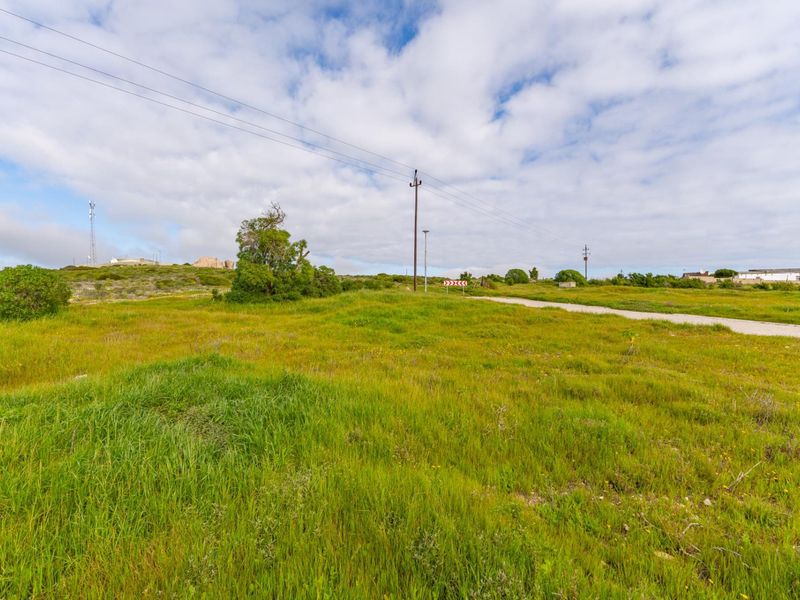 A view of a vacant residential plot featuring natural grass coverage, utility poles, and access to a gravel road.