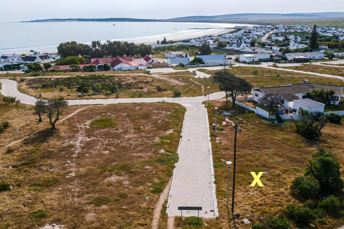 Aerial view of a vacant residential plot featuring paved road access, utility connections, and proximity to the coastline.