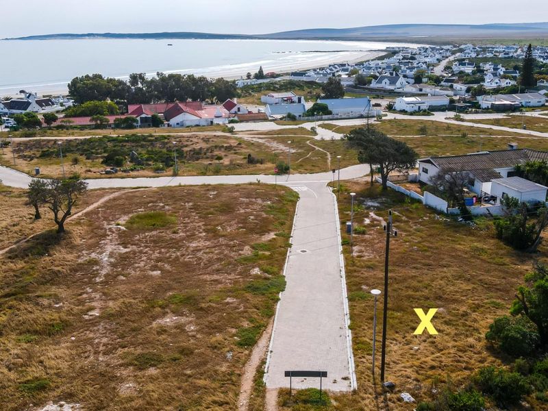 Aerial view of a vacant residential plot featuring paved road access, utility connections, and proximity to the coastline.
