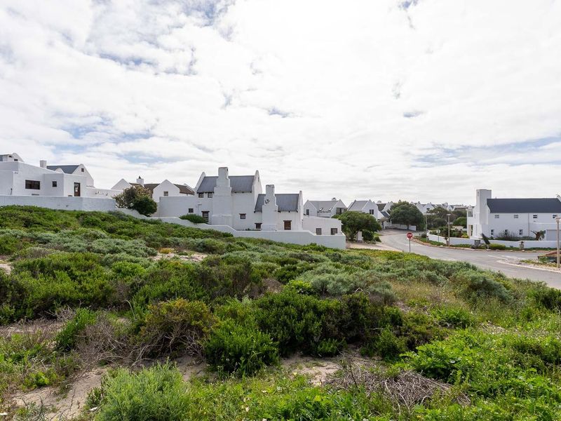 A scenic view of a residential estate featuring white coastal-style homes, native vegetation, and a paved access road.