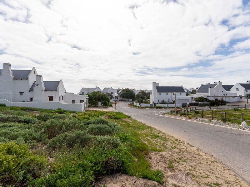 A view of the paved street and surrounding residential neighborhood with coastal vegetation and timber fencing in a well-maintained estate setting.
