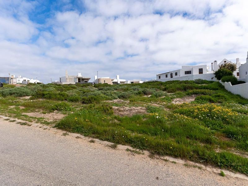 A vacant residential plot of land situated in a coastal development, featuring natural vegetation and direct access to a paved road.