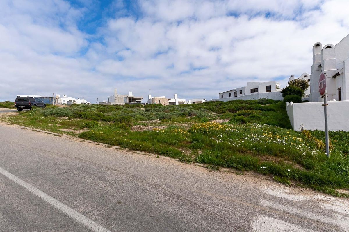 A street-level view of a vacant residential plot situated in a coastal neighborhood, featuring natural vegetation and adjacent established properties.