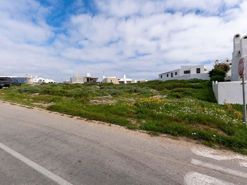 A street-level view of a vacant residential plot situated in a coastal neighborhood, featuring natural vegetation and adjacent established properties.