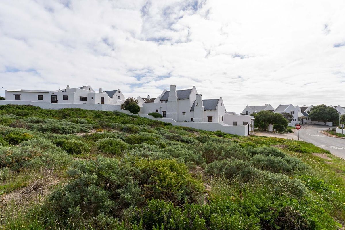 A view of the vacant residential land plot situated in a coastal estate, featuring established vegetation and proximity to the local road network.