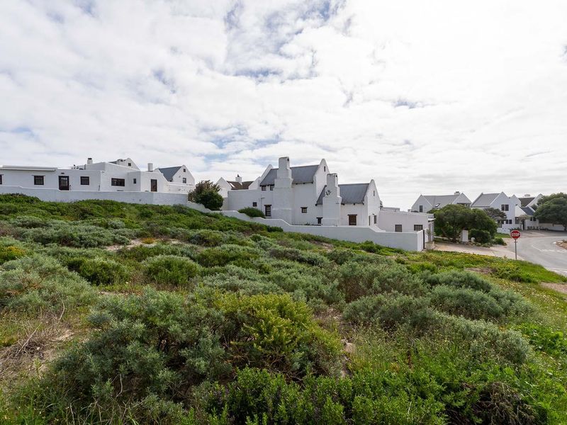 A view of the vacant residential land plot situated in a coastal estate, featuring established vegetation and proximity to the local road network.
