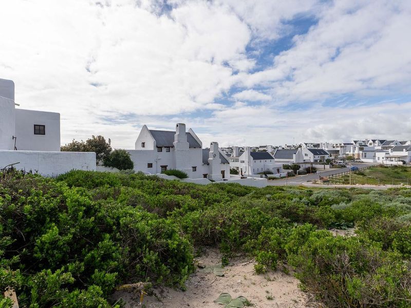 A view of the front elevation of a white coastal residence surrounded by native vegetation in a residential estate setting.