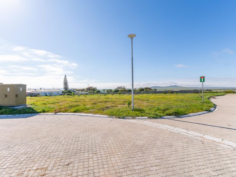 A vacant residential plot featuring paved street access, established curbing, and utility infrastructure, ready for development in a quiet neighborhood setting.