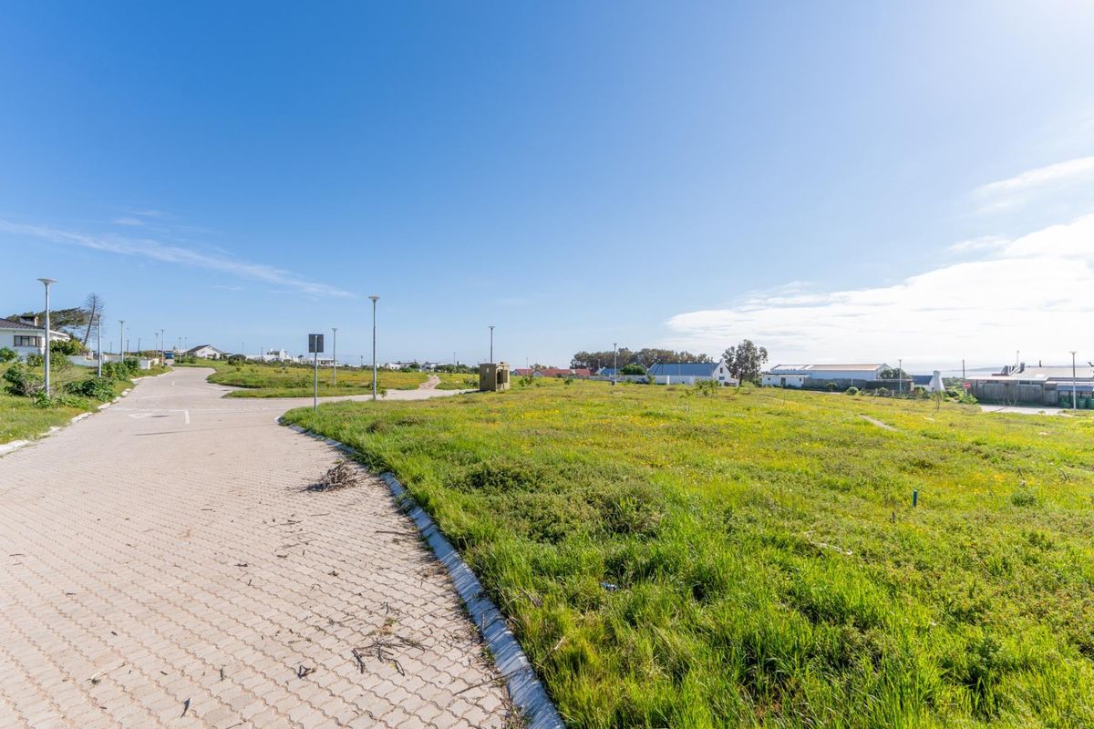 A vacant residential plot featuring a paved driveway, street lighting, and established grass, offering a clear view of the surrounding neighborhood.