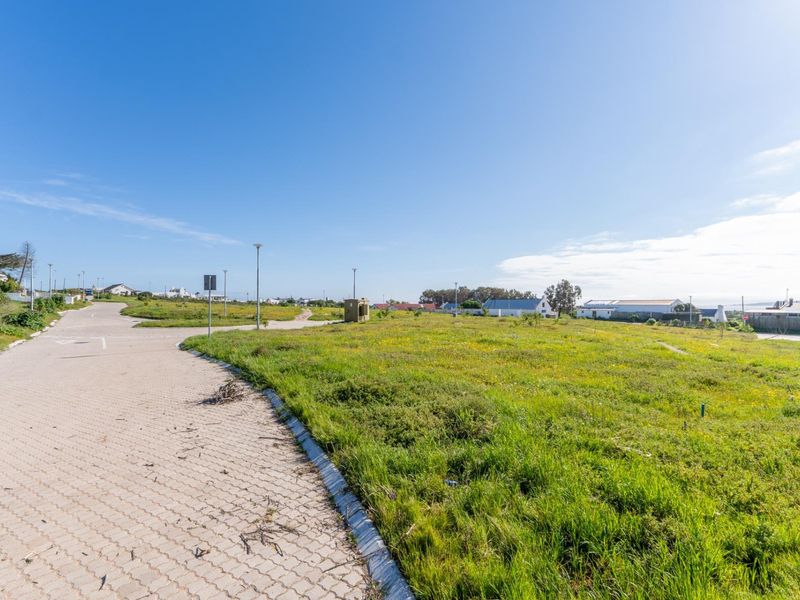 A vacant residential plot featuring a paved driveway, street lighting, and established grass, offering a clear view of the surrounding neighborhood.