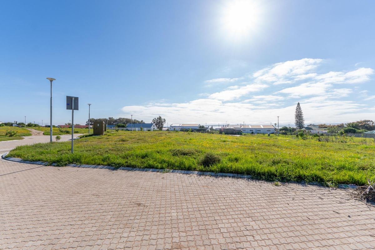 A vacant residential plot featuring a paved driveway, street lighting, and established grass, situated in a developed neighborhood.