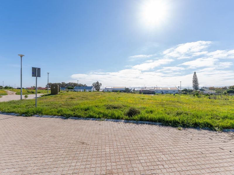A vacant residential plot featuring a paved driveway, street lighting, and established grass, situated in a developed neighborhood.