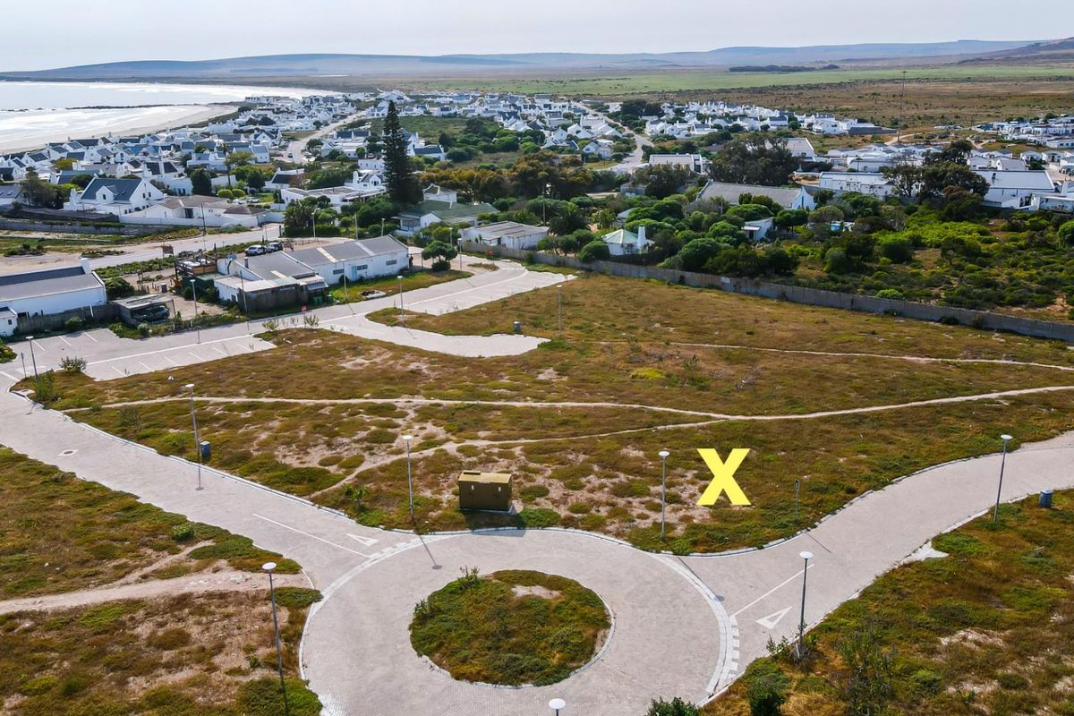 Aerial view of a vacant residential plot featuring a paved roundabout and established street infrastructure in a coastal neighborhood.
