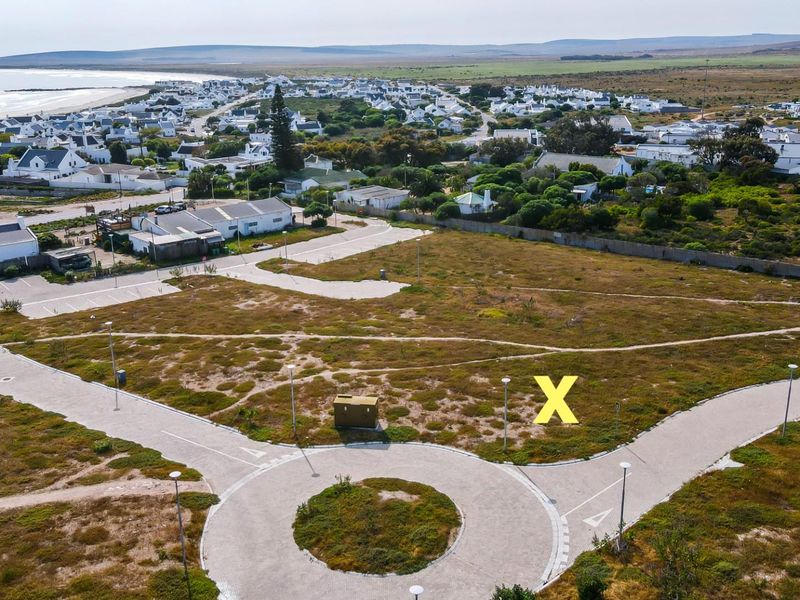 Aerial view of a vacant residential plot featuring a paved roundabout and established street infrastructure in a coastal neighborhood.