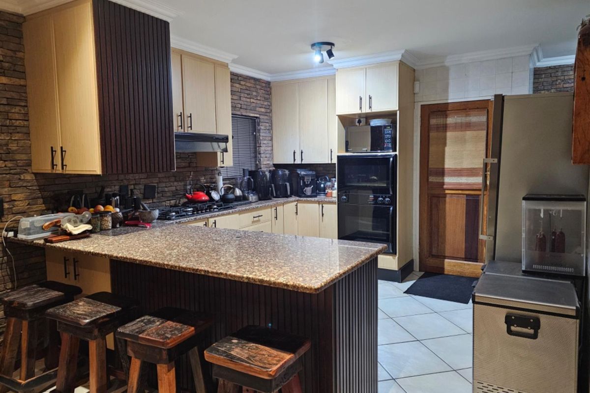 A functional kitchen featuring granite countertops, built-in cabinetry, a gas hob, and a brick veneer feature wall, offering a warm and practical cooking space.