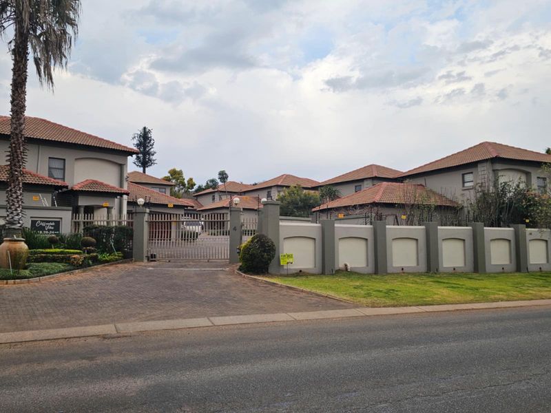 Street view of the townhouse complex entrance featuring a secure gated access point, paved driveway, and perimeter walling.