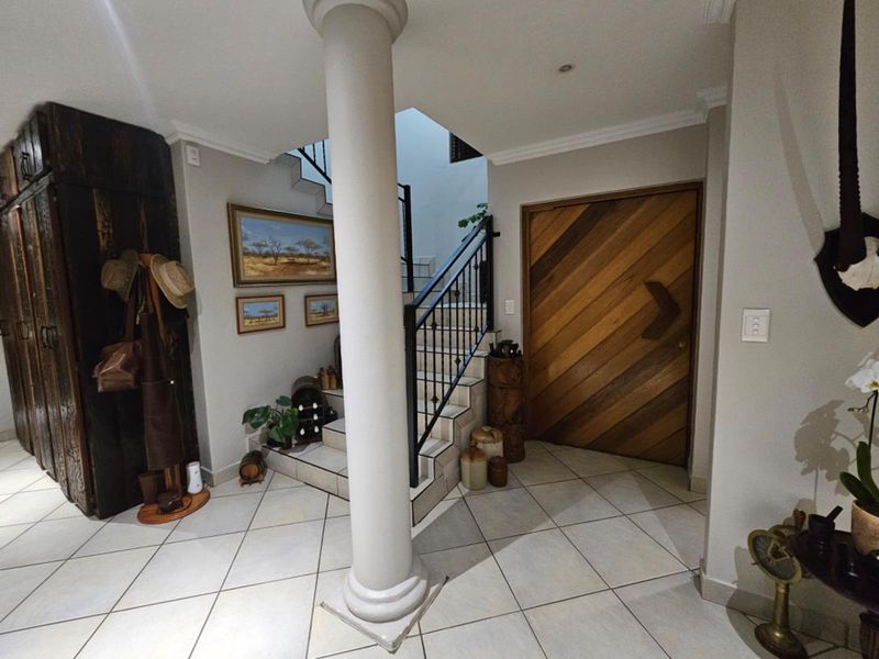 Welcoming entrance foyer featuring tiled flooring, a central structural column, a wooden front door, and a staircase with a wrought iron balustrade.
