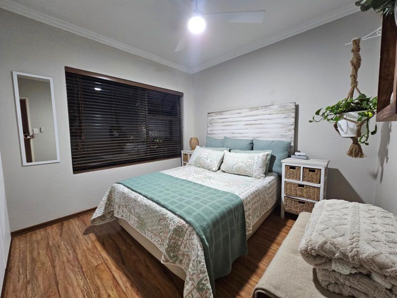 A well-maintained bedroom featuring laminate flooring, a ceiling fan, and venetian blinds, offering a comfortable and functional living space.
