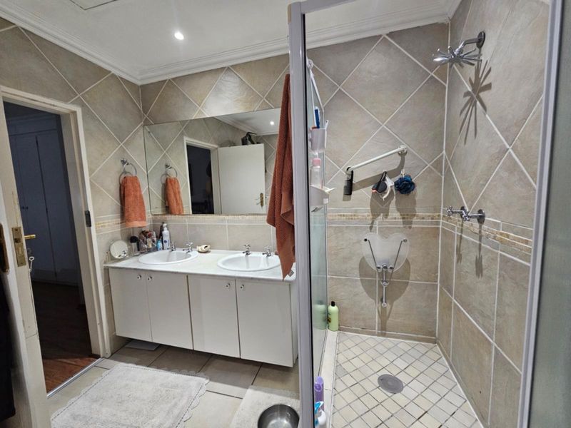 A functional bathroom featuring a double vanity with built-in cabinetry, a glass-enclosed shower, and neutral tiled finishes throughout.