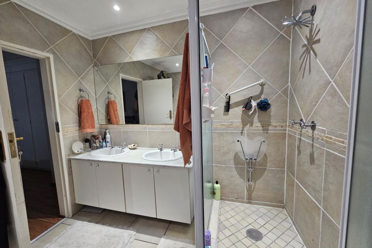 A functional bathroom featuring a double vanity with built-in cabinetry, a glass-enclosed shower, and neutral tiled finishes throughout.