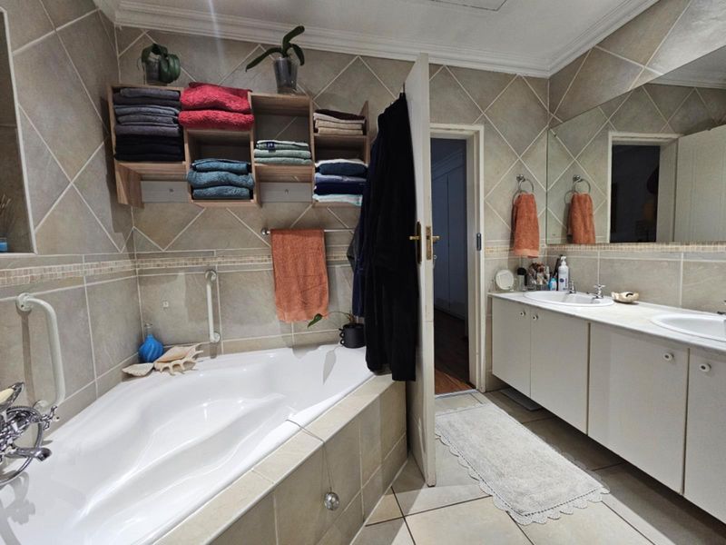 A functional bathroom featuring a corner bathtub, double vanity with integrated sinks, large wall mirror, and neutral tiled finishes throughout.