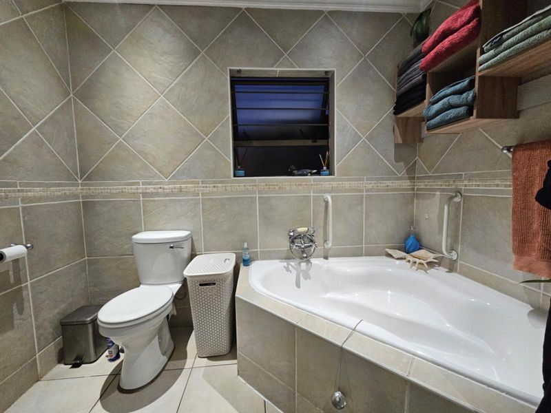 A functional bathroom featuring a corner bathtub, tiled walls with decorative border, toilet, and built-in shelving, providing a practical and well-maintained space.
