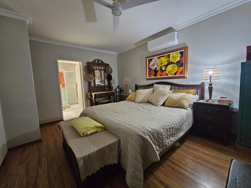 A well-maintained bedroom featuring laminate flooring, a ceiling fan, and a wall-mounted split-system air conditioner, with direct access to an en-suite bathroom.