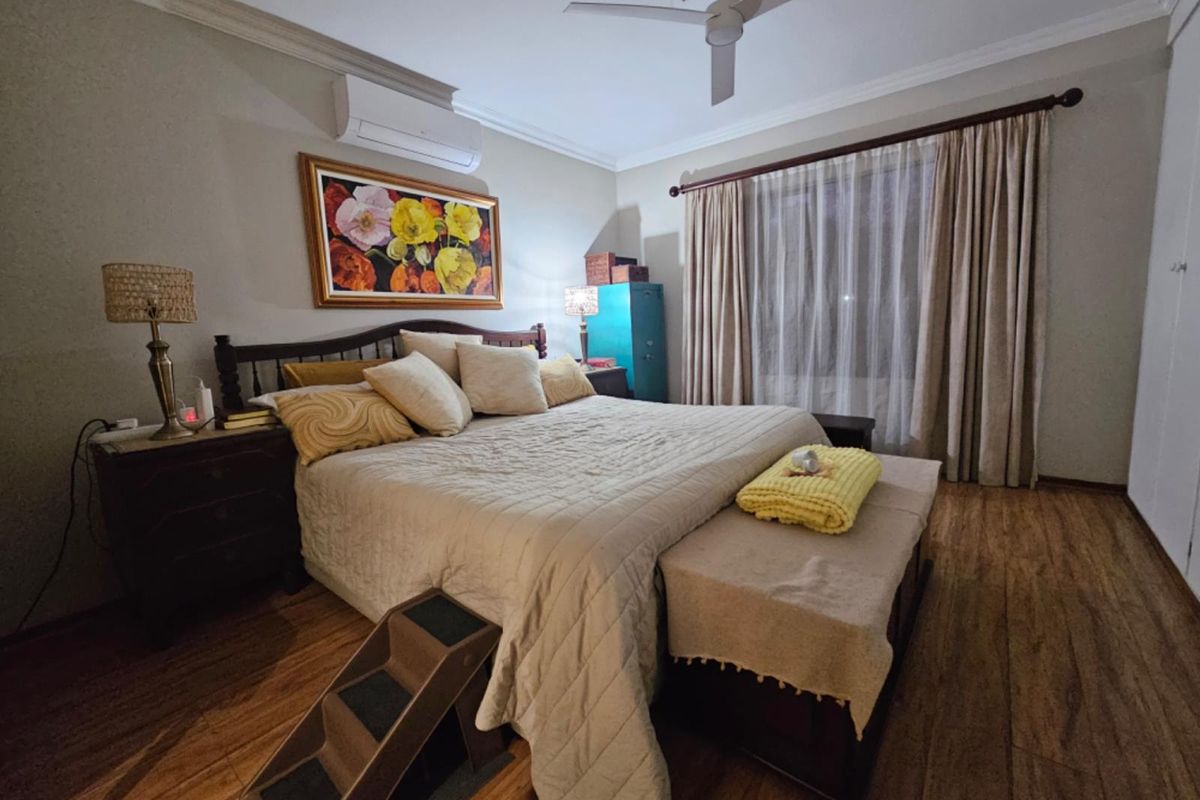A well-maintained bedroom featuring laminate flooring, a ceiling fan, and a wall-mounted split-system air conditioner.