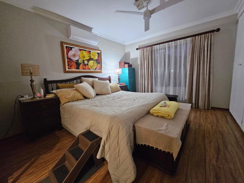 A well-maintained bedroom featuring laminate flooring, a ceiling fan, and a wall-mounted split-system air conditioner.