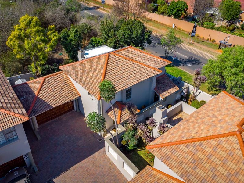 Aerial view of a townhouse property featuring a terracotta tiled roof, paved driveway, and secure boundary walls within a residential estate setting.