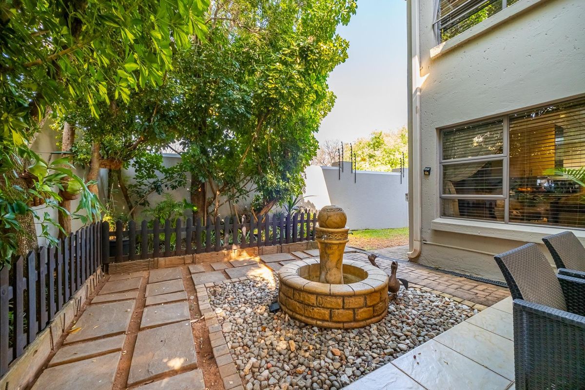 A private rear courtyard featuring stone paving, a decorative water fountain, pebble landscaping, and secure perimeter walling with electric fencing.