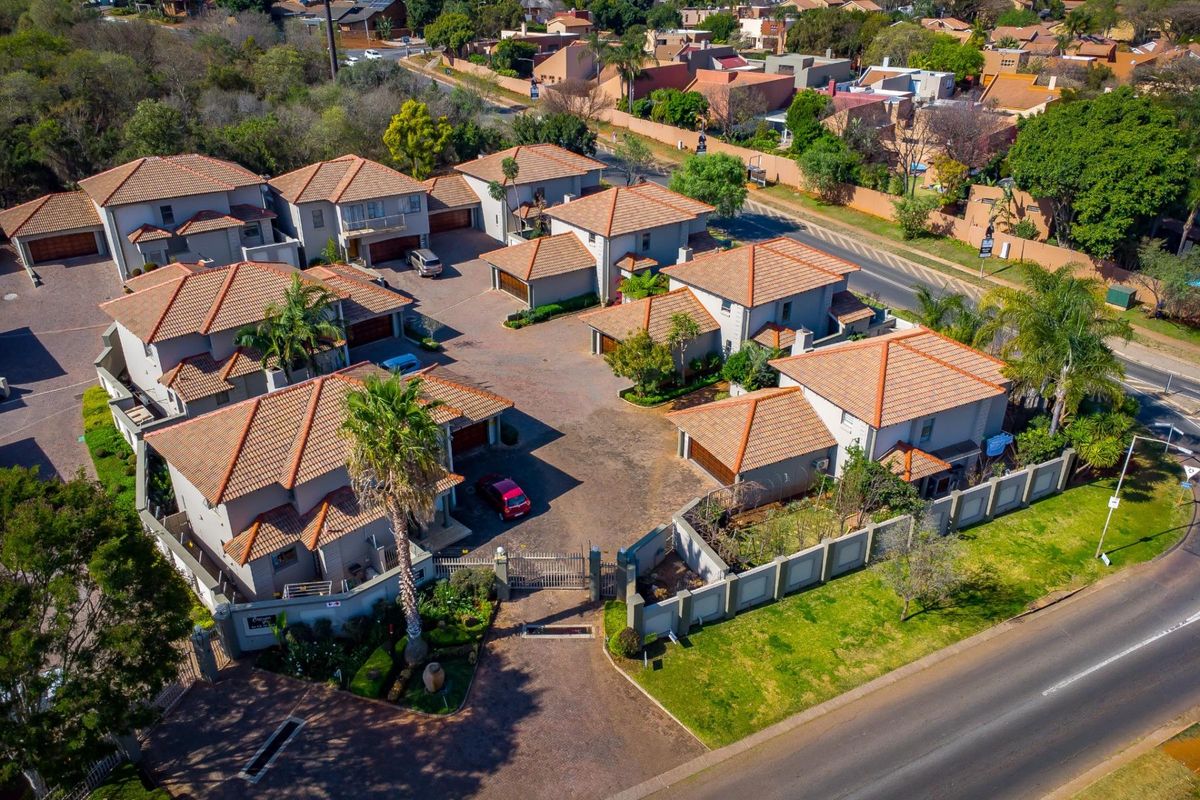 Aerial view of a townhouse complex featuring multiple units with tiled roofs, paved driveways, and secure perimeter walling.