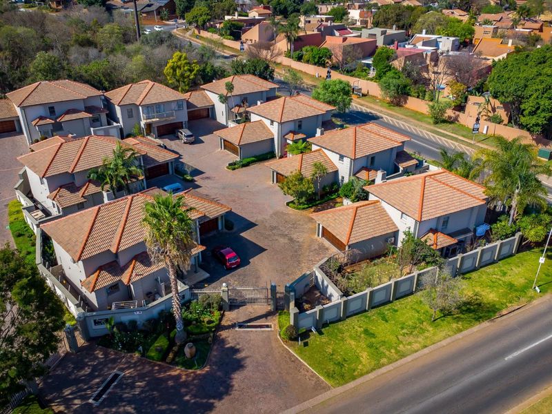 Aerial view of a townhouse complex featuring multiple units with tiled roofs, paved driveways, and secure perimeter walling.