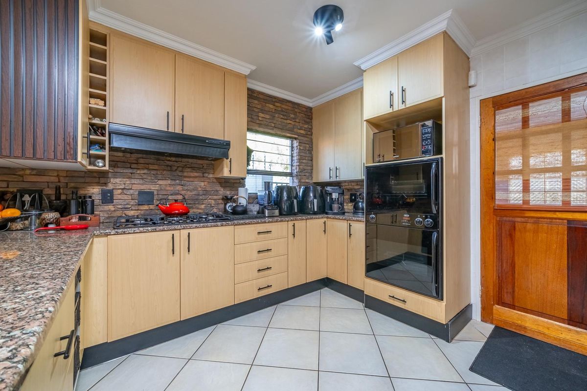 Well-appointed kitchen featuring light wood cabinetry, granite countertops, stone veneer backsplash, and integrated appliances including a gas hob and built-in oven.