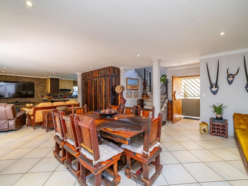 Spacious open-plan living and dining area featuring tiled floors, recessed lighting, a feature brick wall, and an integrated staircase.