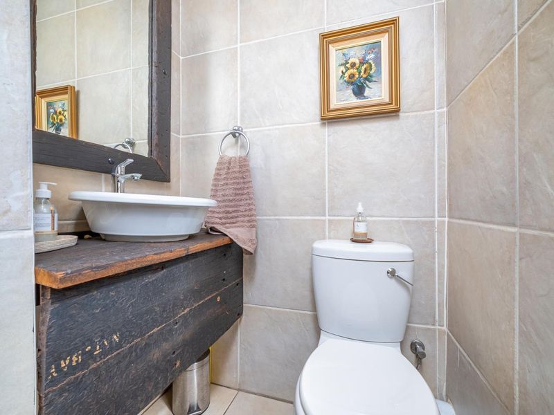 A compact bathroom featuring a vessel sink on a rustic wooden vanity, a ceramic toilet, and neutral wall tiling.