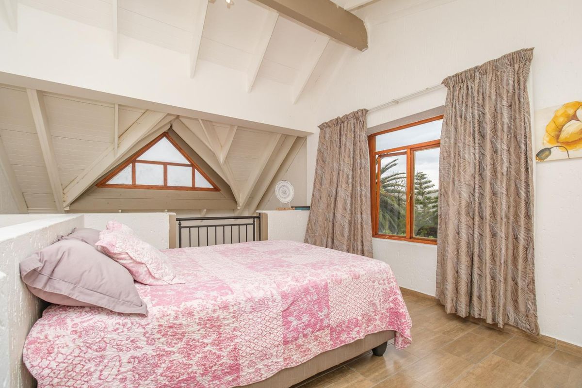 A cozy loft-style bedroom featuring exposed timber rafters, a vaulted ceiling, and large timber-framed windows that provide natural light and exterior views.