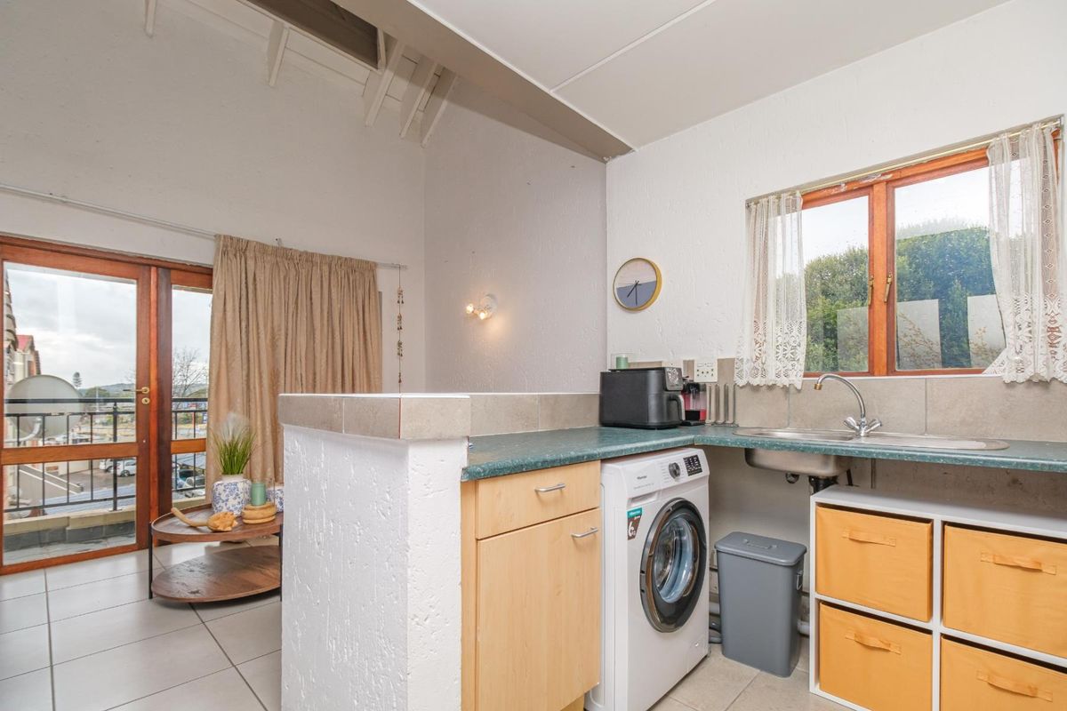 Compact kitchen area featuring laminate countertops, stainless steel sink, tiled backsplash, and built-in cabinetry, with direct access to an adjacent balcony.