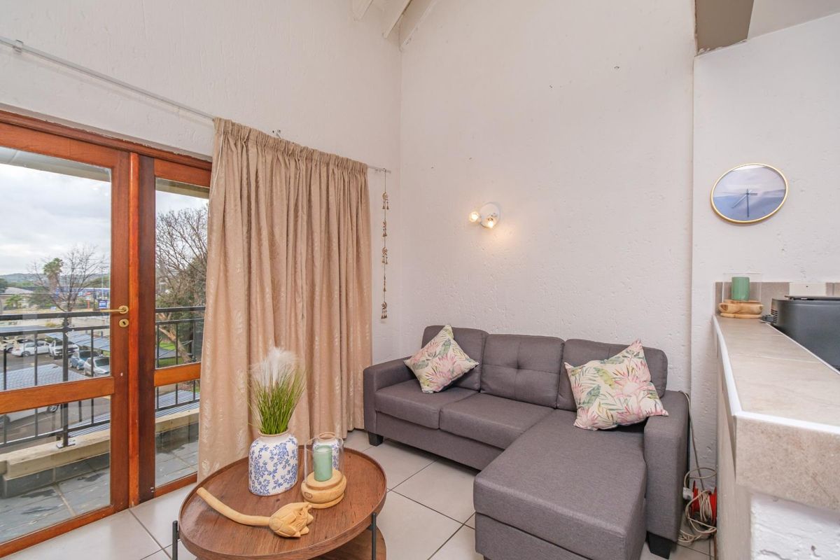 A compact living area featuring tiled floors, a high vaulted ceiling, and a timber-framed sliding door providing access to an outdoor balcony.