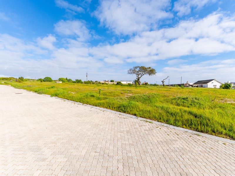 A view of a vacant residential plot featuring a paved road and concrete curbing, ready for development.