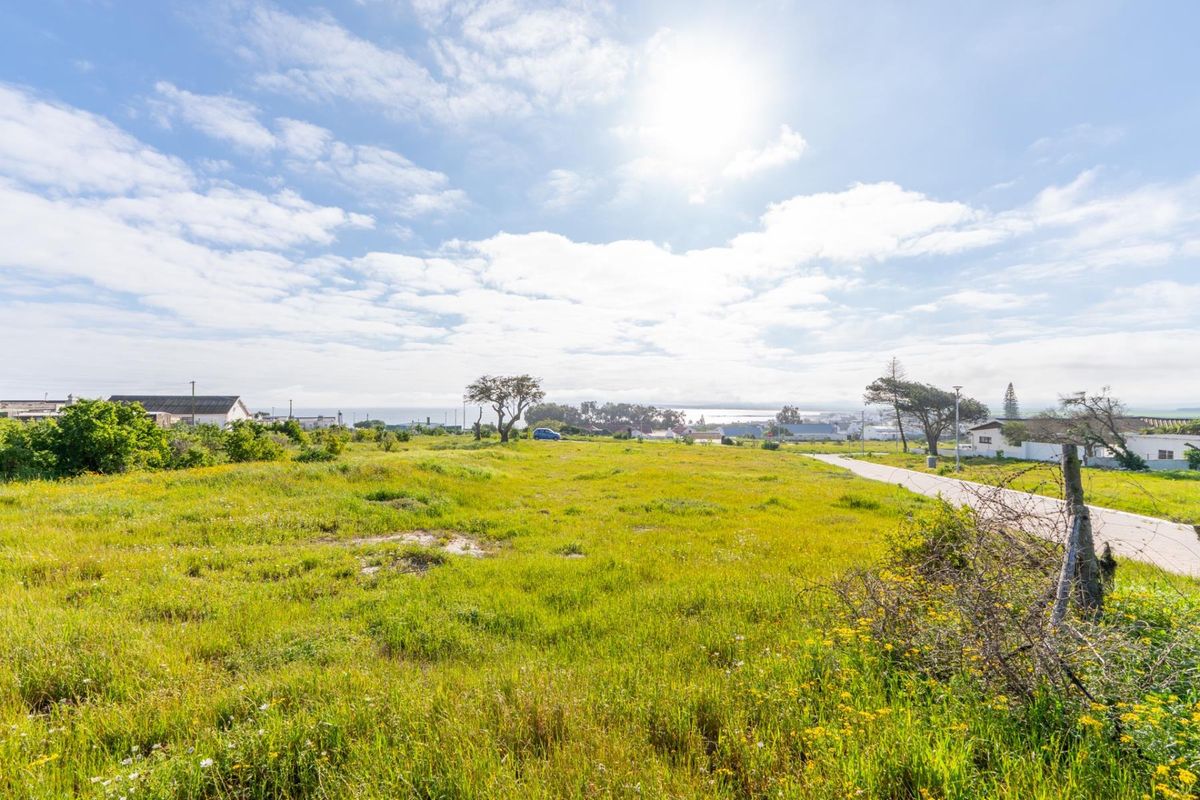 A vacant residential plot featuring open grassland with road access and distant coastal views, suitable for new development.