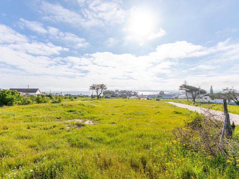 A vacant residential plot featuring open grassland with road access and distant coastal views, suitable for new development.