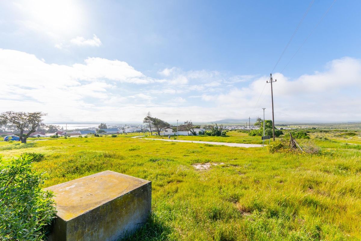 A vacant residential plot featuring natural grass coverage, a utility pole, and a concrete plinth, offering expansive views of the surrounding landscape.