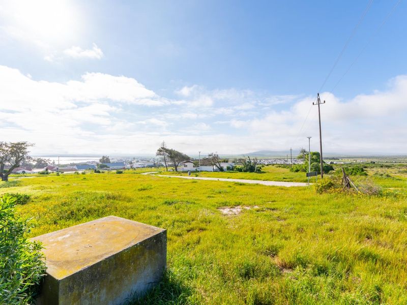 A vacant residential plot featuring natural grass coverage, a utility pole, and a concrete plinth, offering expansive views of the surrounding landscape.