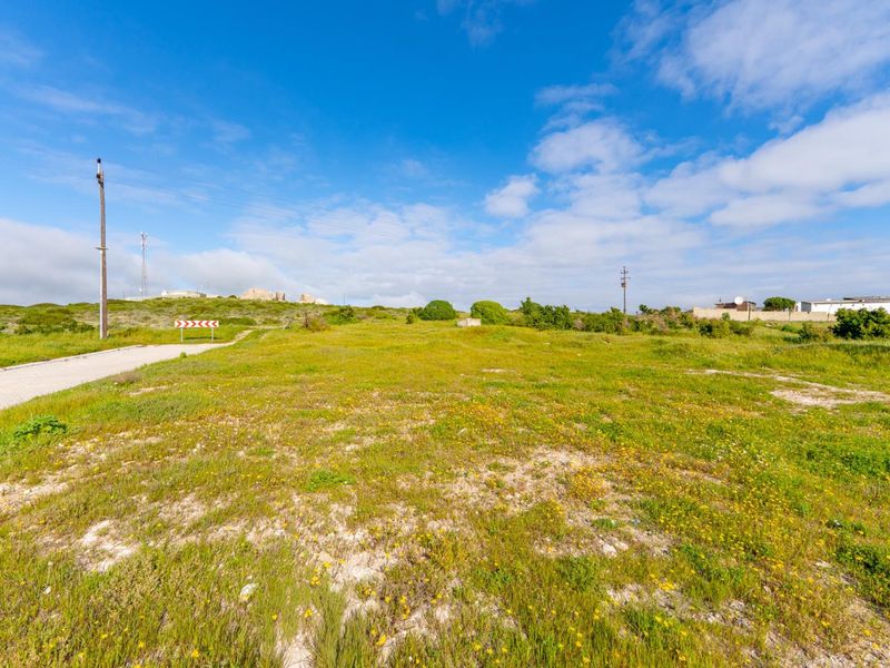 A vacant residential plot featuring natural vegetation, a paved access road, and utility infrastructure, offering a clear site for future development.