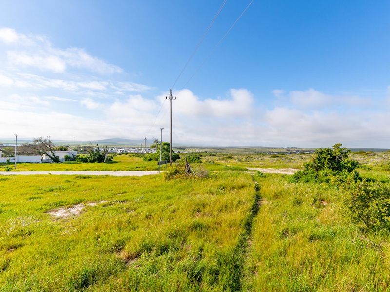 A view of a vacant residential plot featuring natural grass coverage, a utility pole, and access to a paved road.