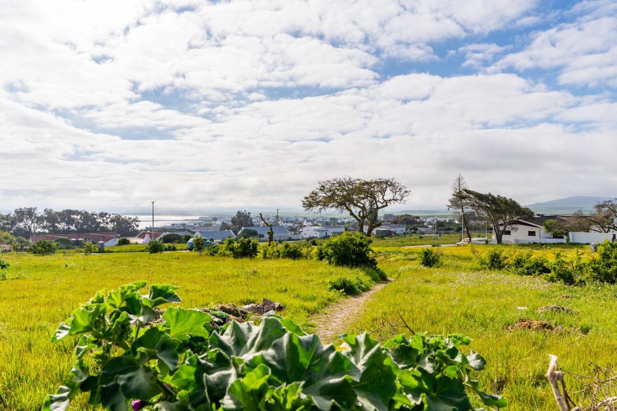 A scenic view overlooking a grassy vacant residential plot with surrounding neighborhood and distant coastal landscape.