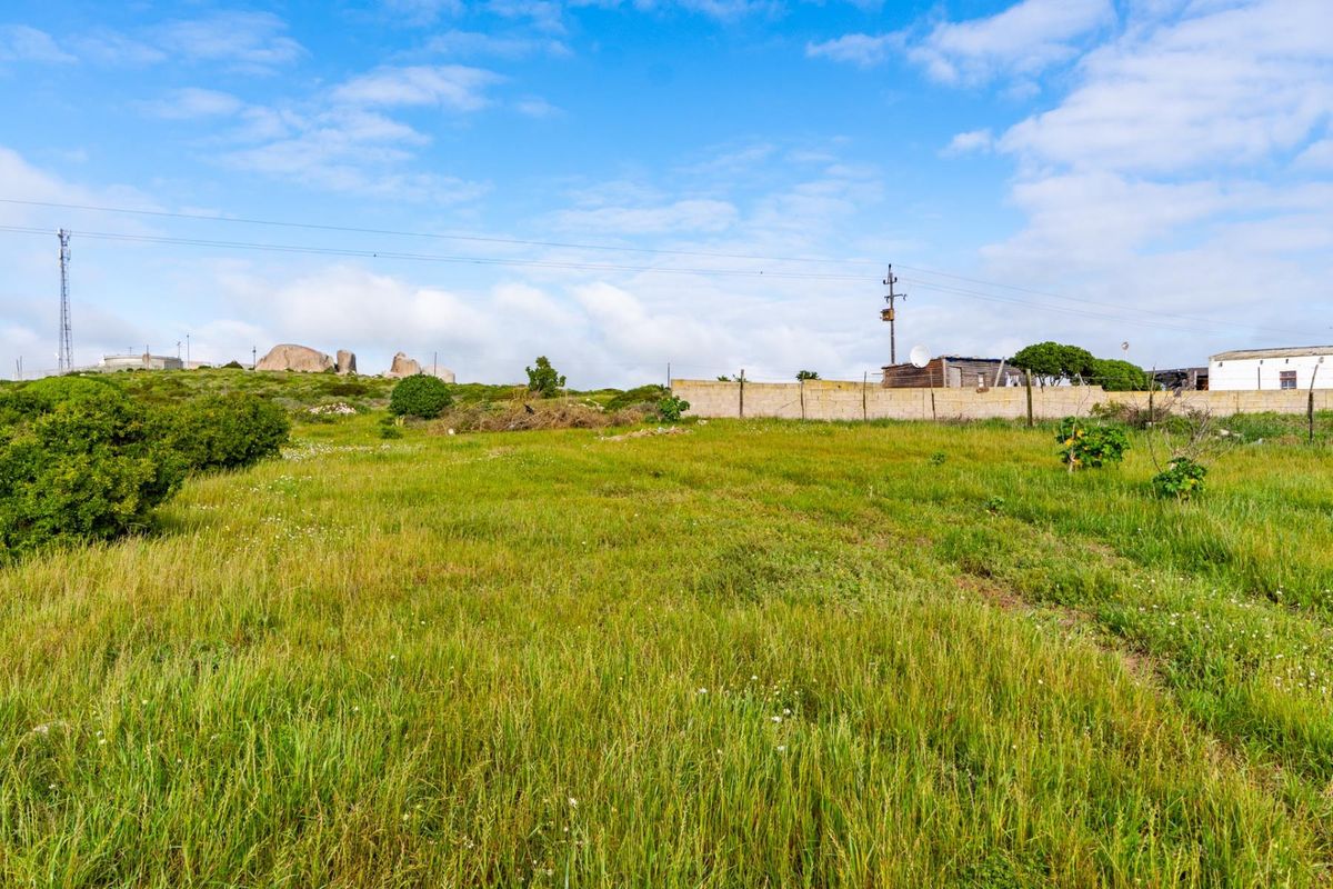 A view of a vacant residential plot featuring natural grass coverage, a boundary wall, and surrounding landscape.