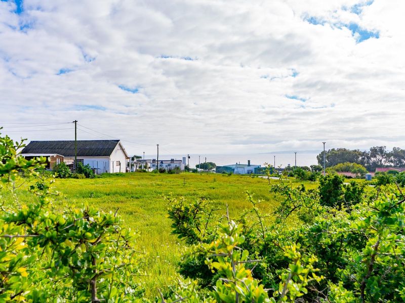 A scenic view of a vacant residential plot featuring natural grassland with distant coastal views and surrounding neighborhood infrastructure.