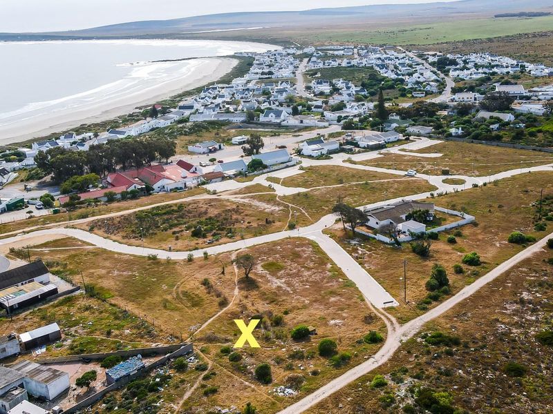 Aerial view of a vacant residential plot situated in a coastal development, featuring proximity to the beach and established road access.